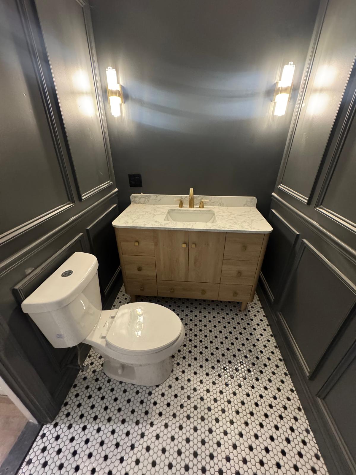Powder room — charcoal paneled walls, oak vanity, marble top and brass fixtures